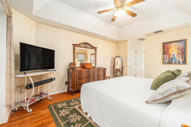 bedroom with a tray ceiling, wood finished floors, visible vents, and baseboards