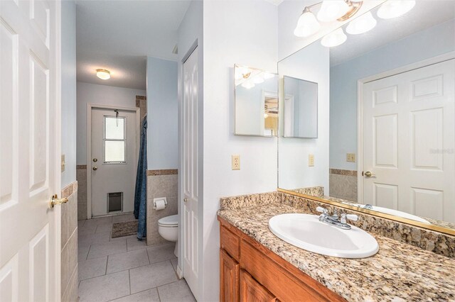 full bathroom featuring tile patterned flooring, toilet, vanity, tile walls, and a closet