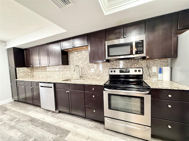 kitchen with a tray ceiling, stainless steel appliances, tasteful backsplash, a sink, and dark brown cabinetry