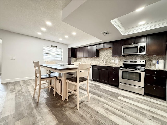 kitchen featuring dark brown cabinetry, tasteful backsplash, appliances with stainless steel finishes, and a tray ceiling