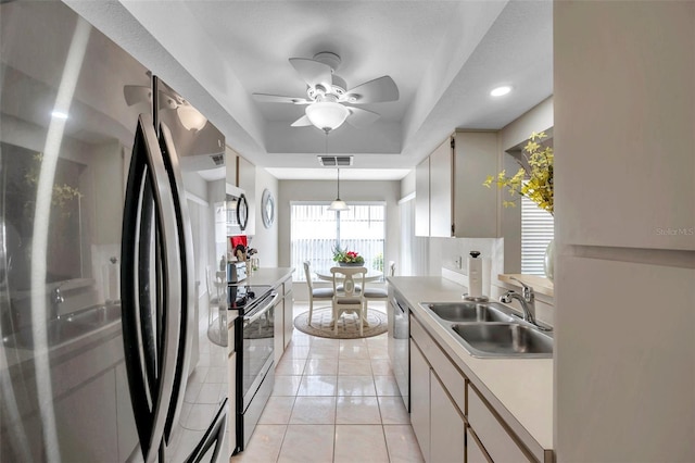 kitchen with appliances with stainless steel finishes, sink, light tile patterned floors, pendant lighting, and a tray ceiling