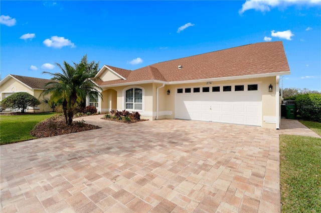 ranch-style home featuring a shingled roof, decorative driveway, an attached garage, and stucco siding