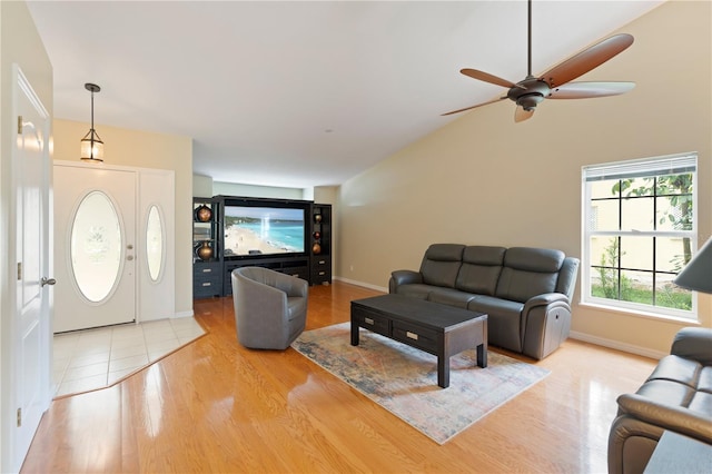 living area featuring light wood-type flooring, baseboards, vaulted ceiling, and a ceiling fan