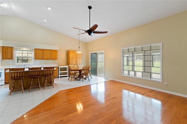 unfurnished dining area with light wood-style floors, baseboards, high vaulted ceiling, and ceiling fan with notable chandelier