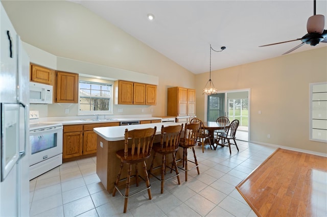 kitchen with light tile patterned floors, white appliances, a kitchen island, a sink, and light countertops