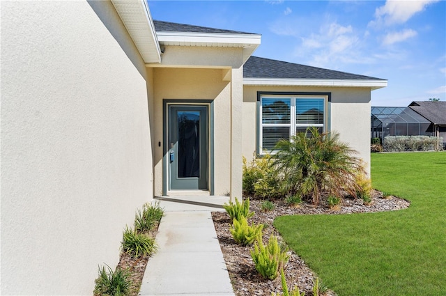 entrance to property featuring a shingled roof, a lawn, and stucco siding