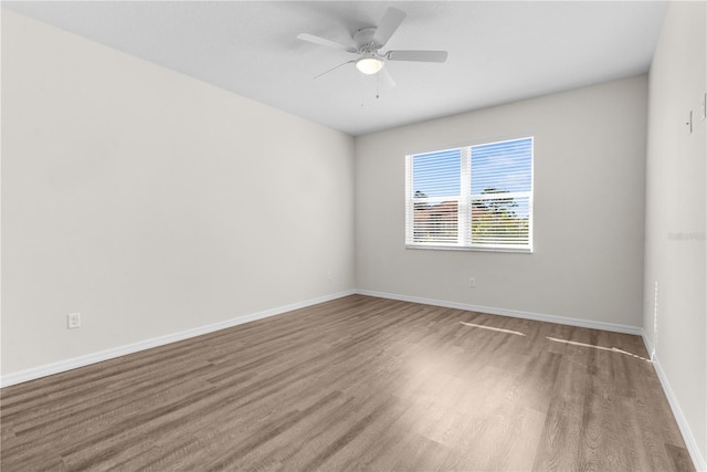 spare room with wood finished floors, a ceiling fan, and baseboards