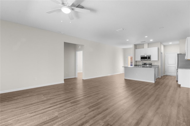 unfurnished living room featuring a sink, ceiling fan, baseboards, and wood finished floors