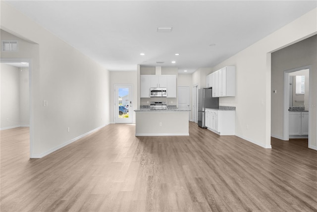 kitchen with stainless steel appliances, a kitchen island with sink, open floor plan, and white cabinetry