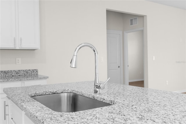 kitchen featuring light stone counters, a sink, visible vents, baseboards, and white cabinetry