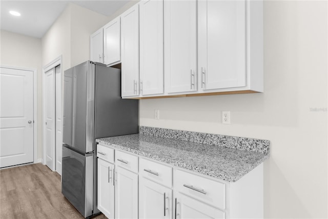 kitchen with recessed lighting, light wood-style floors, freestanding refrigerator, white cabinetry, and light stone countertops