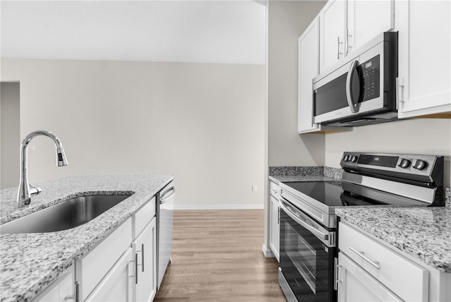 kitchen featuring light stone countertops, white cabinetry, stainless steel appliances, and a sink