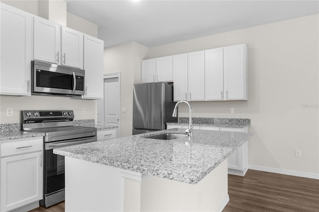 kitchen featuring white cabinets, an island with sink, light stone counters, stainless steel appliances, and a sink