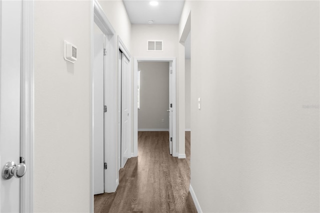 hallway featuring dark wood-type flooring, visible vents, and baseboards