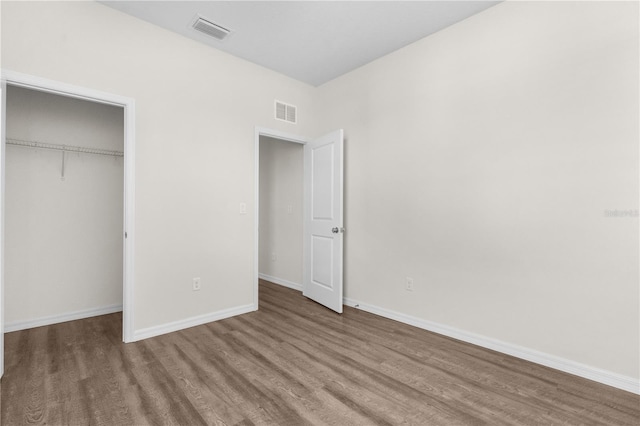 unfurnished bedroom featuring baseboards, a closet, visible vents, and wood finished floors