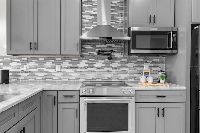 kitchen featuring stainless steel appliances, wall chimney range hood, decorative backsplash, and gray cabinetry