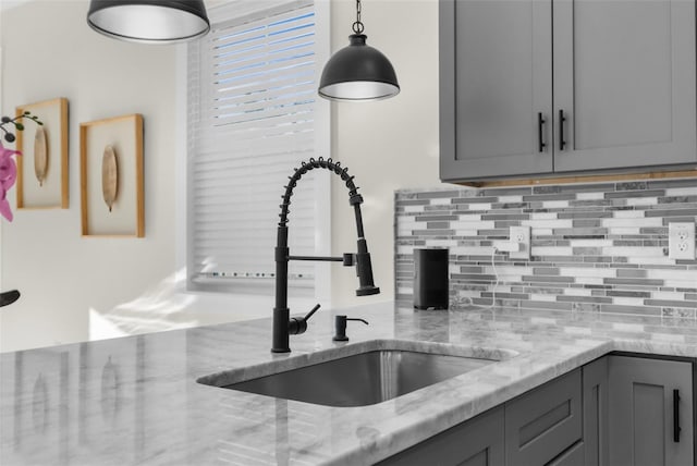 kitchen featuring tasteful backsplash, light stone counters, gray cabinetry, pendant lighting, and a sink