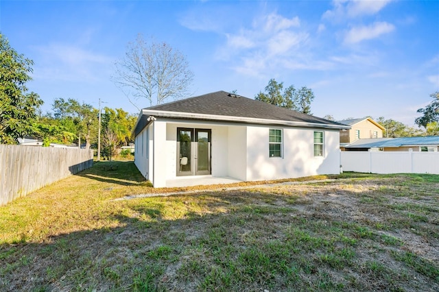 rear view of property with a fenced backyard, roof with shingles, a lawn, and stucco siding