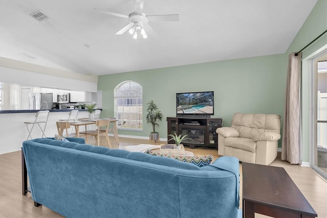 living area with light wood finished floors, visible vents, vaulted ceiling, ceiling fan, and baseboards