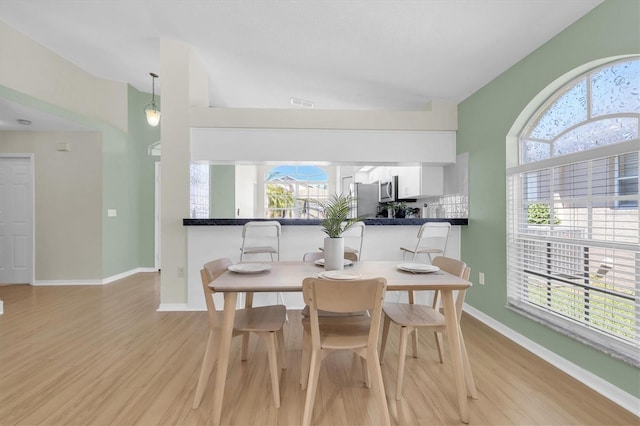 dining space featuring vaulted ceiling, light wood finished floors, visible vents, and baseboards