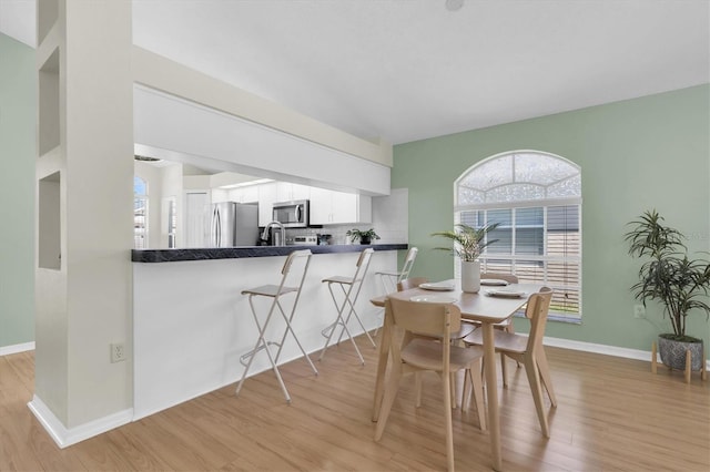 dining space featuring light wood-style floors, baseboards, and vaulted ceiling