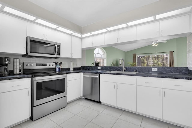 kitchen with light tile patterned floors, stainless steel appliances, a sink, white cabinets, and backsplash