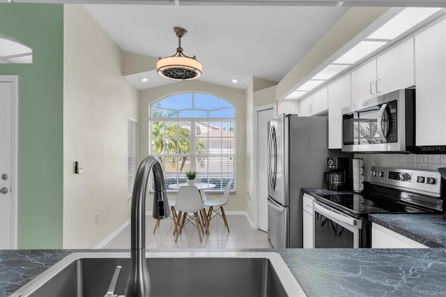 kitchen featuring stainless steel appliances, dark countertops, lofted ceiling, white cabinets, and a sink