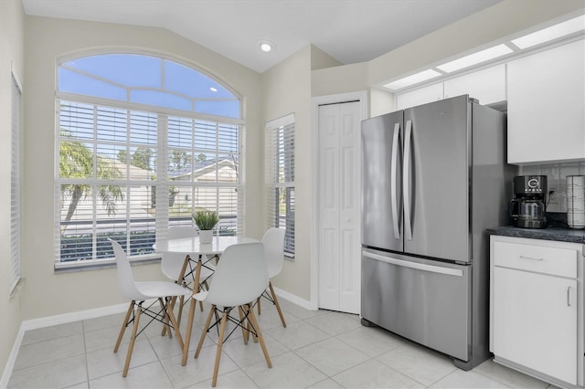 kitchen with light tile patterned floors, baseboards, dark countertops, freestanding refrigerator, and white cabinetry