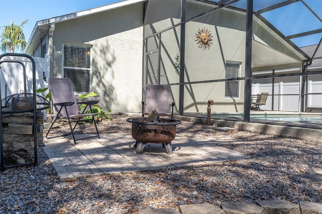 view of patio / terrace featuring glass enclosure, an outdoor fire pit, fence, and an outdoor pool