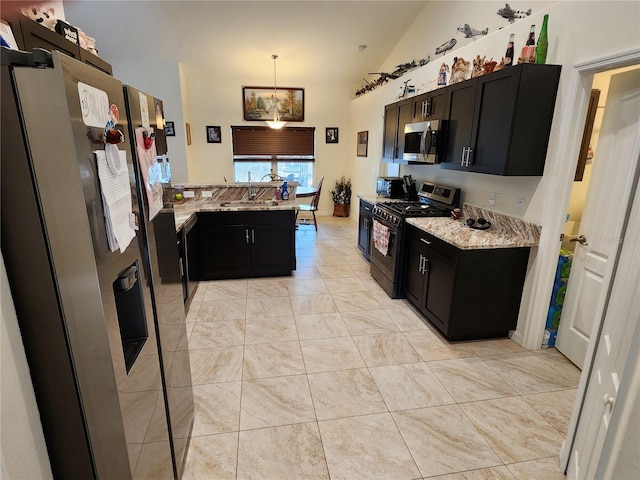 kitchen featuring light stone counters, dark cabinets, a sink, appliances with stainless steel finishes, and pendant lighting