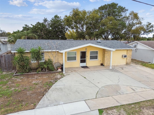 ranch-style home featuring a shingled roof, fence, an AC wall unit, stone siding, and stucco siding