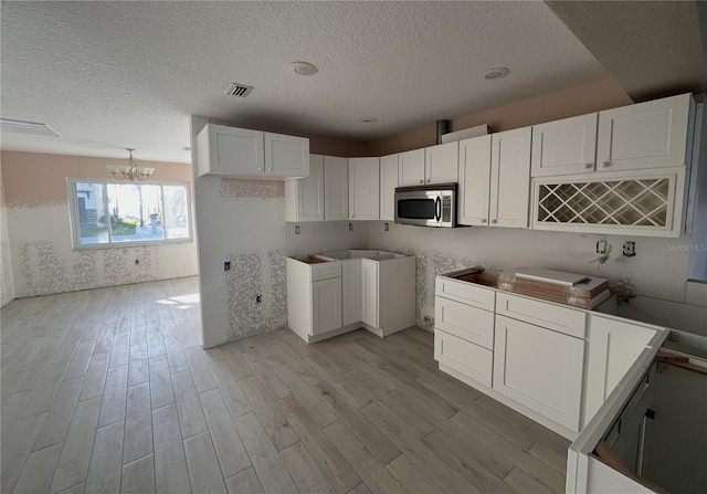6228 Lonnie Lee Ln, Hudson, FL 34667 - kitchen with stainless steel microwave, light wood-type flooring, a textured ceiling, a chandelier, and white cabinetry