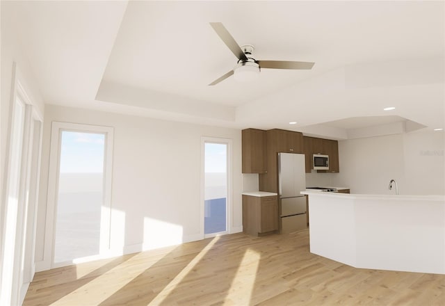 kitchen with light wood finished floors, a tray ceiling, light countertops, and white appliances