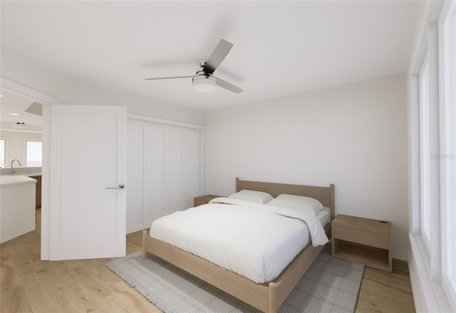 bedroom featuring light wood finished floors, ceiling fan, a closet, and a sink