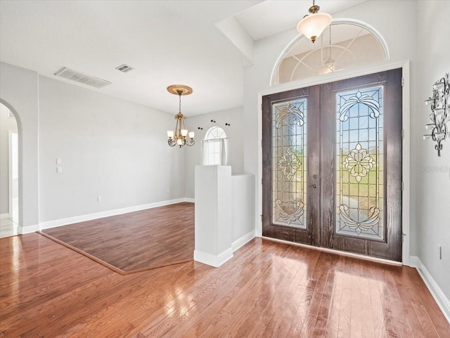 foyer entrance with arched walkways, french doors, visible vents, and wood finished floors