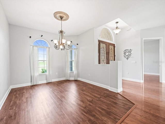 unfurnished room with baseboards, wood finished floors, and an inviting chandelier