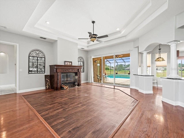 unfurnished living room featuring ceiling fan, dark wood-type flooring, visible vents, baseboards, and a tray ceiling