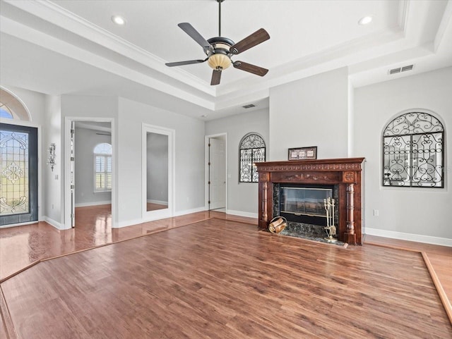 unfurnished living room with baseboards, visible vents, a fireplace with flush hearth, wood finished floors, and a tray ceiling