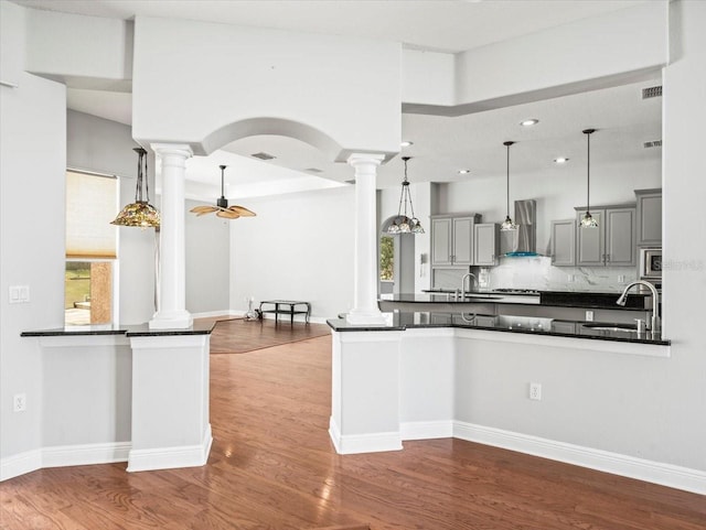 kitchen featuring dark countertops, gray cabinetry, decorative columns, and wall chimney exhaust hood