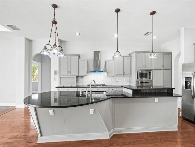 kitchen with arched walkways, stainless steel appliances, wall chimney range hood, and a large island