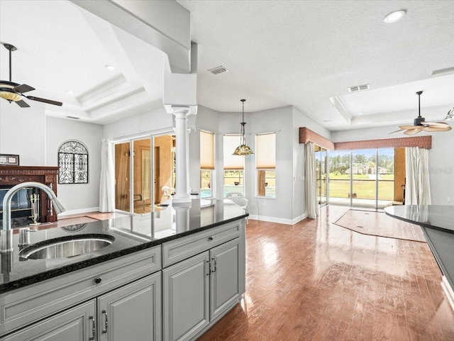 kitchen featuring decorative columns, dark stone countertops, a tray ceiling, gray cabinetry, and a sink