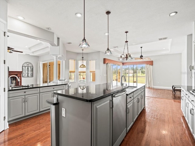 kitchen with gray cabinets, a tray ceiling, dark countertops, a center island with sink, and pendant lighting