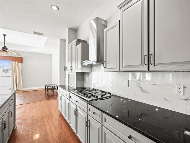 kitchen with gray cabinets, visible vents, stainless steel gas stovetop, and wall chimney exhaust hood