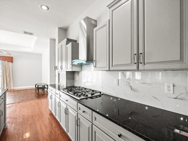 kitchen with stainless steel gas cooktop, wall chimney range hood, and gray cabinetry