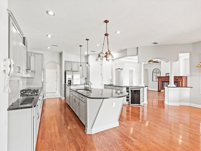 kitchen featuring arched walkways, a center island with sink, hanging light fixtures, and decorative columns