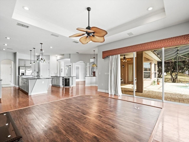 unfurnished living room with visible vents, arched walkways, ceiling fan, and a tray ceiling