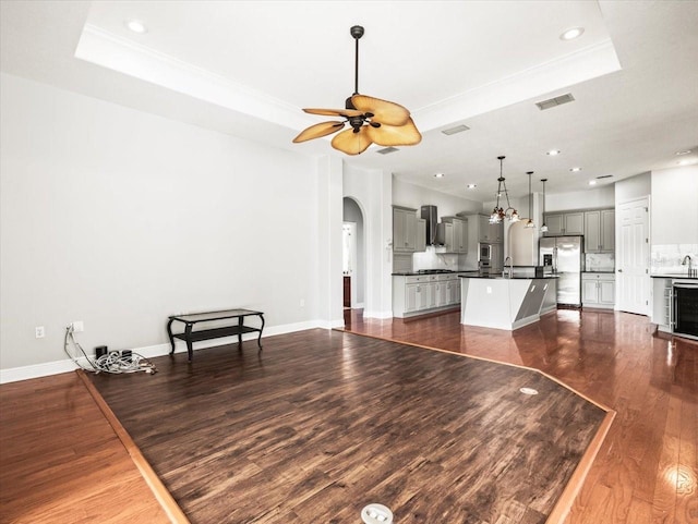 living area with arched walkways, dark wood-style flooring, visible vents, a ceiling fan, and a raised ceiling