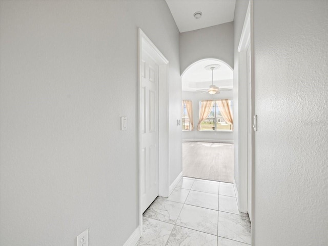 corridor featuring marble finish floor, baseboards, and arched walkways