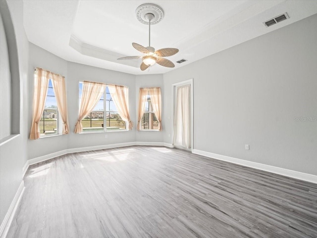 unfurnished room with a tray ceiling, visible vents, baseboards, and wood finished floors