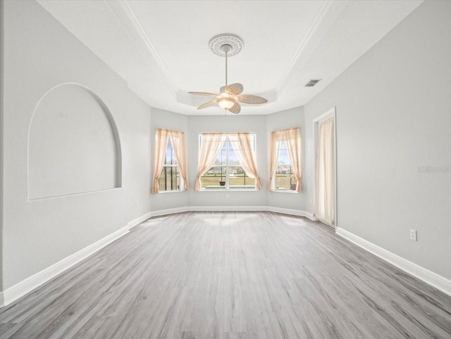 unfurnished room with ceiling fan, light wood-style flooring, visible vents, baseboards, and a raised ceiling